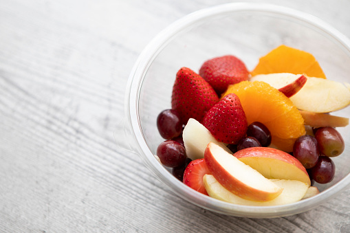 Ready-made, take-away fruit salad, in a plastic container, on a wooden table