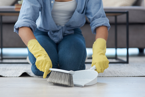Shot of an anonymous woman using a dustpan and sweeping her living room floor at home