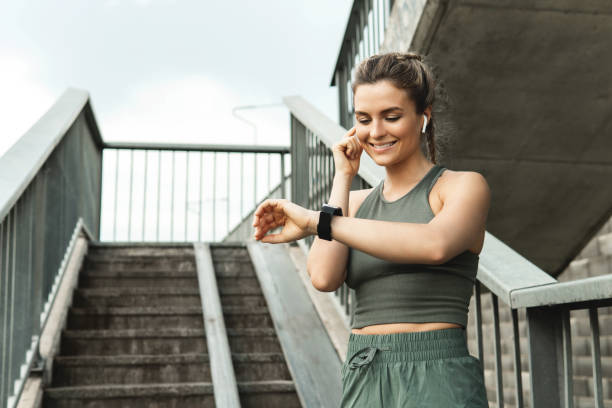 mujer atlética usando reloj inteligente durante su entrenamiento de fitness en la calle de la ciudad - body building exercises audio fotografías e imágenes de stock