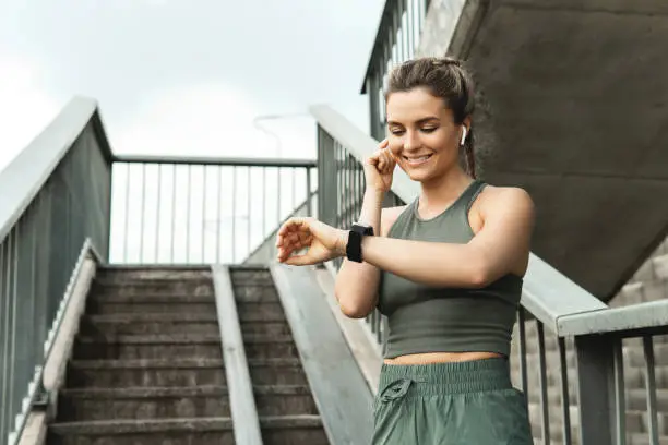 Young athletic woman using smartwatch during her fitness workout on city street