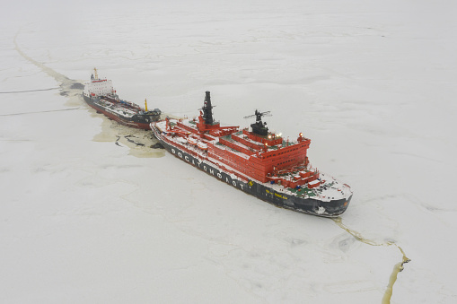 Sabetta, Tyumen region, Russia - April 4, 2021: The 50 let Pobedy icebreaker towing a tanker on the ice. Overcast, light snow is falling.