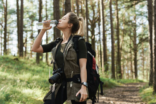 istock Female hiker drinking water from reusable bottle in green forest 1316803497