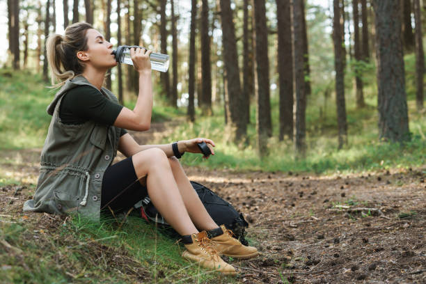 Female hiker drinking water from reusable bottle in green forest