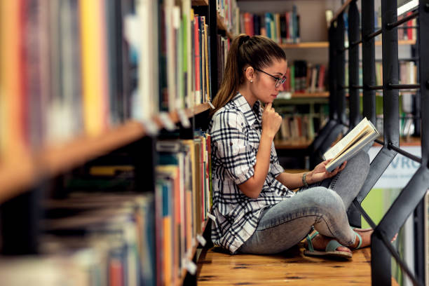 istock Young female student study in the library reading book while sitting near bookshelf. 1316804318