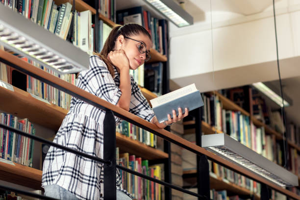 istock Young female student study in the library reading book while sitting near bookshelf. 1316804374