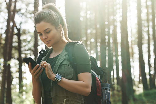 Young female hiker is using smartphone for navigation in green forest