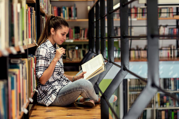 istock Young female student study in the library reading book while sitting near bookshelf. 1316805680