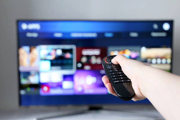 istock Smart TV remote controller in female hand on screen background 1316807419