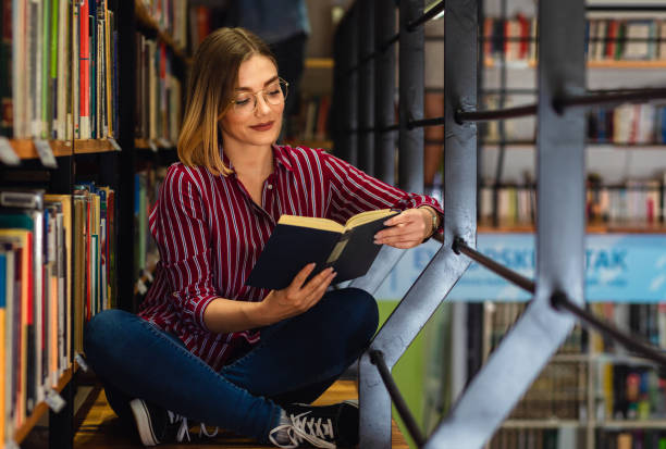 istock Young female student study in the library reading book sitting near bookshelf. 1316808051