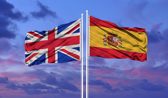 United Kingdom and Spain flag waving in the wind against white cloudy blue sky together. Diplomacy concept, international relations