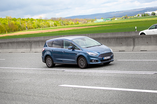 Diedenbergen, Germany - May 06, 2021: A middle-aged man in a blue FORD S-Max on a highway nearby Wiesbaden, Germany. The Ford S-Max is an MPV produced by Ford Europe for the European market. Ford of Europe GmbH is a subsidiary company of Ford Motor Company founded in 1967 in Cork, Ireland