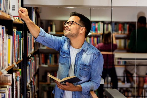 istock Young male student study in the library reading book near bookshelf. 1316808773