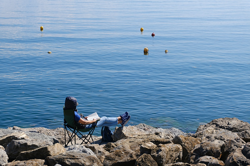 Istanbul, Turkey - April 21, 2021 : A modern young woman is reading her book on rocks and enjoying the sun at Suadiye coastline.