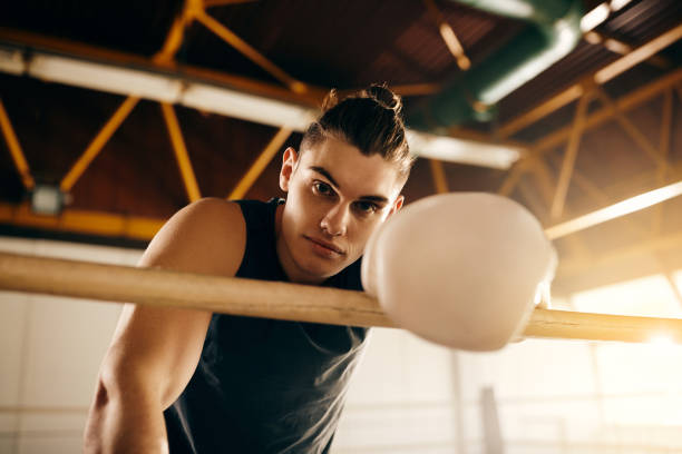 istock Young male fighter leaning on ropes in boxing ring and looking at camera. 1316817566