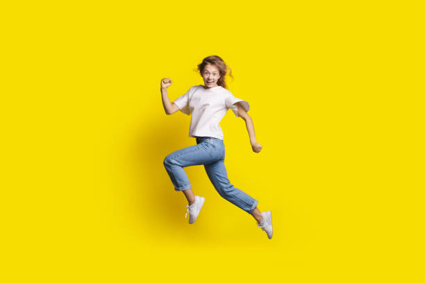 istock Crazy woman is jumping in a yellow studio wall smiling at camera gesturing a run 1316820279