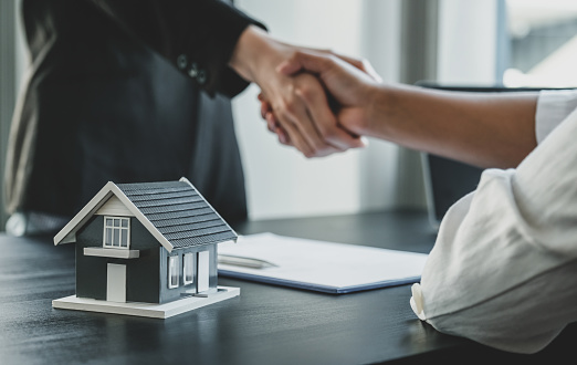 Home model. Real estate agents and buyers handshake after signing a business contract, renting, buying, mortgage, loan or home insurance.