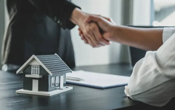 Home model. Real estate agents and buyers handshake after signing a business contract, renting, buying, mortgage, loan or home insurance.