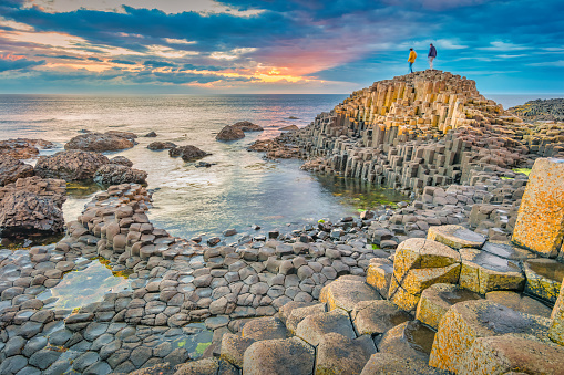 People explore the coast at the landmark Giant's Causeway in Northern Ireland during a dramatic sunset.