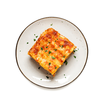 Portion of ground beef lasagne topped with melted cheese and garnished with fresh parsley served on a gray plate . top view. isolated on white background