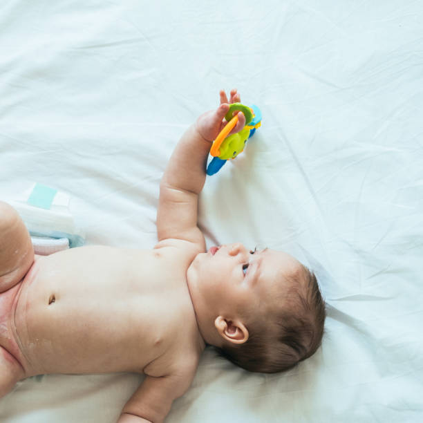 istock Cute Baby Holding Rattle Toy in Hand on White Sheets with Copy Space 1316834272