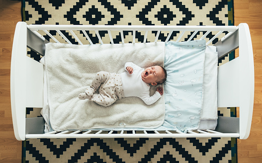 Portrait of a little baby boy waking up after napping in his crib.