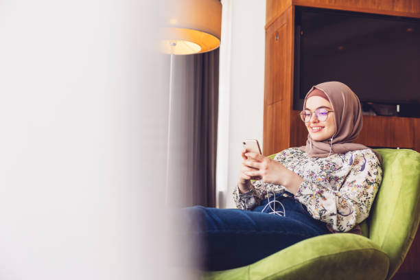 スマートフォンを使って音楽を聴く中東の女の子 - armchair comfortable relaxation headphones ストックフォトと画像