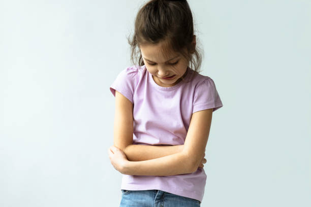 Abdominal Pain Unrecognizable little girl is holding her belly with her two hands because of abdominal pain. gastroenteritis stock pictures, royalty-free photos & images