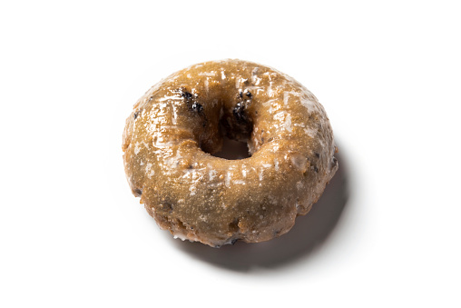 Tabletop photograph of a delicious, blueberry cake donut on a white background. The donut is in the center of the frame.
