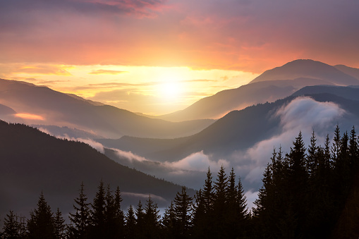 Sunset landscape of high mountain peaks and foggy valley under vibrant colorful evening sky.