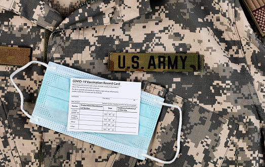 Covid 19 vaccination record card and personal facemask on US Army military uniform.  Individual record for use during the covid 19 coronavirus global pandemic