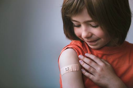 Portrait of a smiling little child with adhesive bandage on his hand after COVID-19 vaccine. Smile on the plaster. Hope concept.