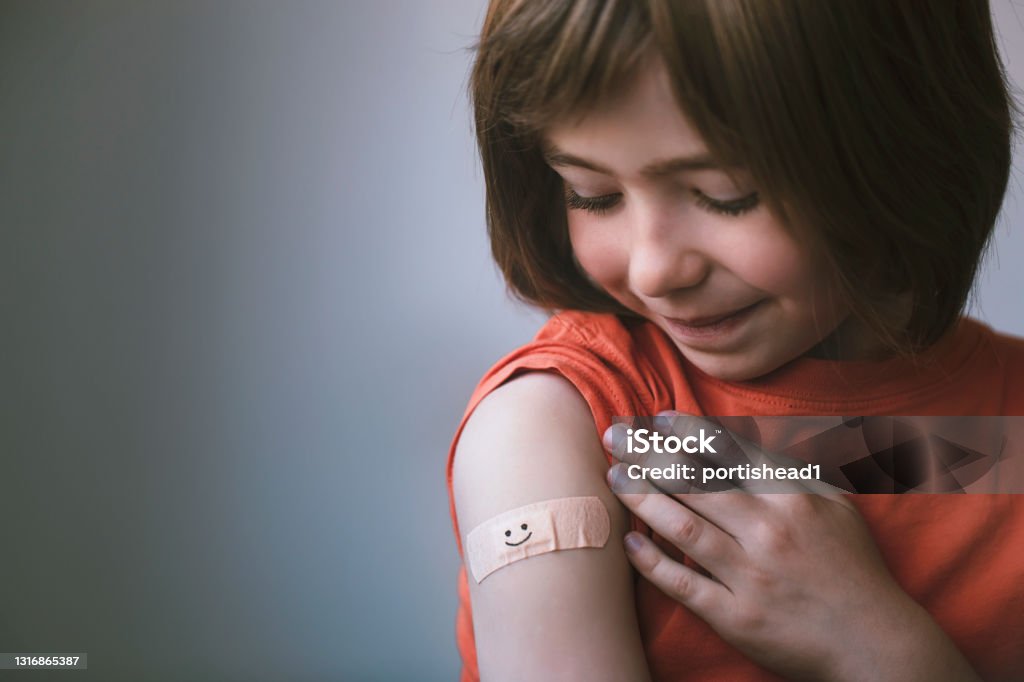 Portrait of smiling little child with adhesive bandage on his hand after vaccination Portrait of a smiling little child with adhesive bandage on his hand after COVID-19 vaccine. Smile on the plaster. Hope concept. Child Stock Photo