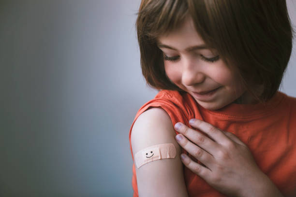 Portrait of smiling little child with adhesive bandage on his hand after vaccination Portrait of a smiling little child with adhesive bandage on his hand after COVID-19 vaccine. Smile on the plaster. Hope concept. injecting stock pictures, royalty-free photos & images