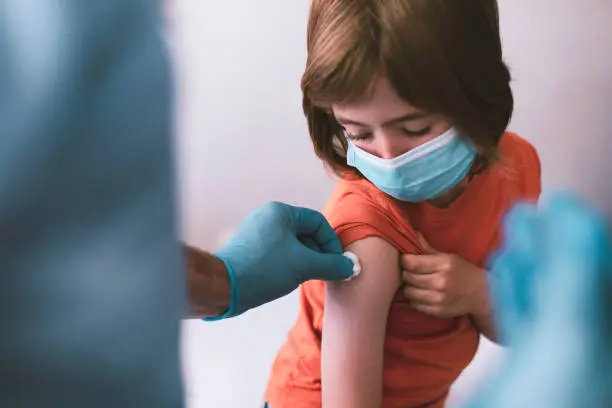 Doctor vaccinating a little child. Doctor wearing protective workwear injecting vaccine into patient's arm.