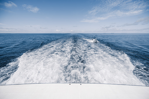 View from the boat stern of the wake (wash) effect on the water from the motor placed on the transom of a luxury safari vessel cruising between Maldives islands with a tied tiny dinghy behind