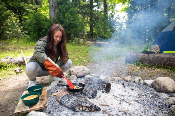 A man lighst a fire in the yard beneath an iron campfire grill pan. This outdoor scene captures a rustic cooking tradition, hands-on learning, and quality family time in nature.