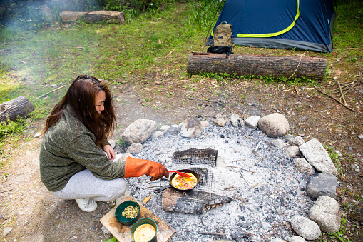 A Japanese lady cooking an omelette over hot coals of a camp fire in an iron skillet at her camp site in the wilderness by her self.