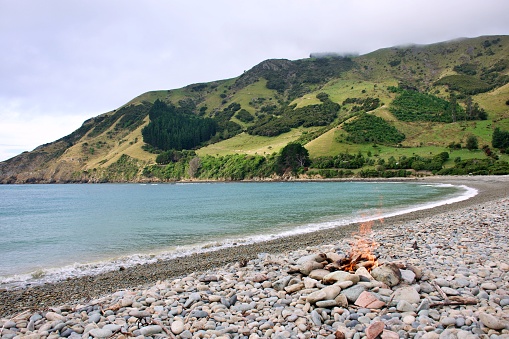A campfire burns on a stoney beach shore. Taken at Cable Bay in the Nelson Region of New Zealand's South Island.