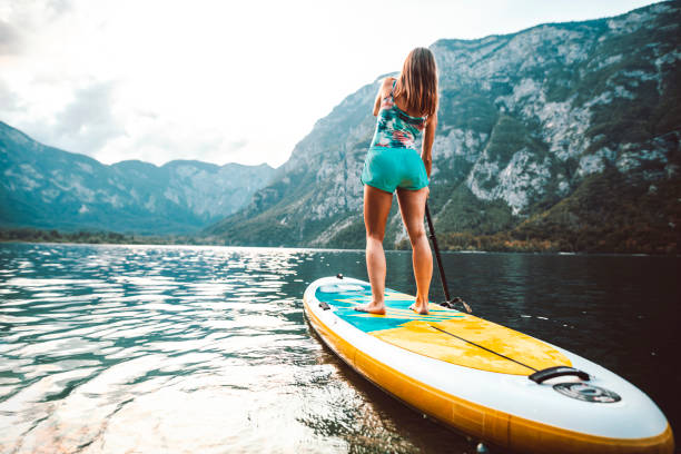 Woman Paddleboarding on Lake in Scenic Triglav National Park Mid adult Caucasian woman moving past camera while paddleboarding on Lake Bohinj with view of Julian Alps. paddleboard surfing water sport low angle view stock pictures, royalty-free photos & images