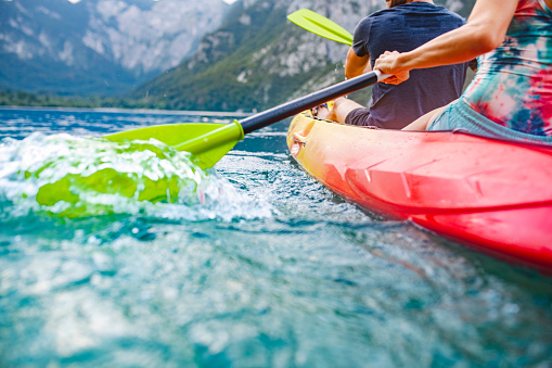 Low angle view of mid adult Caucasian couple paddling kayak past camera as they cross lake in Triglav National Park with Julian Alps in background.