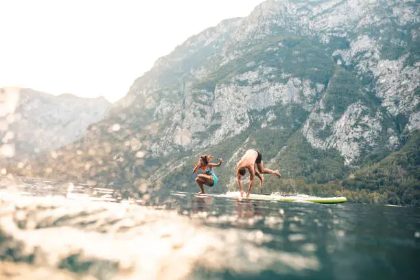 Photo of Vacationing Couple Jumping Off Paddleboard into Lake Bohinj