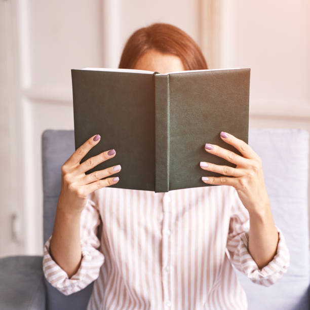 istock Young woman sitting at chair. Hide face behind notebook 1316878210