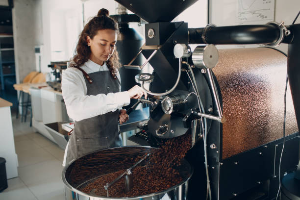 istock Coffee cooling in roaster machine at coffee roasting process. Young woman worker barista Mixing coffee beans. 1316878229