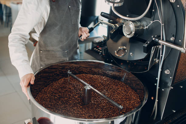 istock Coffee cooling in empty roaster machine at coffee roasting process. Young woman worker pours out coffee beans. 1316878231