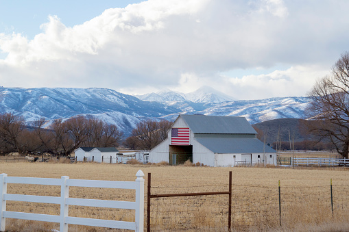 This shot shows snow covered mountains and a valley in Wallsburg, Utah.  This shot was taken in the early spring when snow had melted in the valley meadows but not on the mountain peaks.  Also visible is a barn with an American Flag.