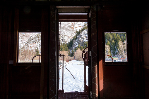 This shot shows snow covered mountains and a valley as seen from the rear windows of a caboose on a railroad track.