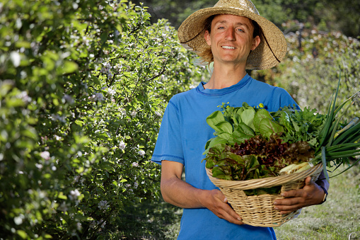 Man in California standing in apple orchard holding basket of vegetables looking at camera.