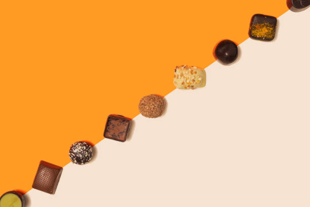 Lovely delicious and colorful chocolate truffles and pralines aligned in diagonal against bright orange and light pink flat lay composition