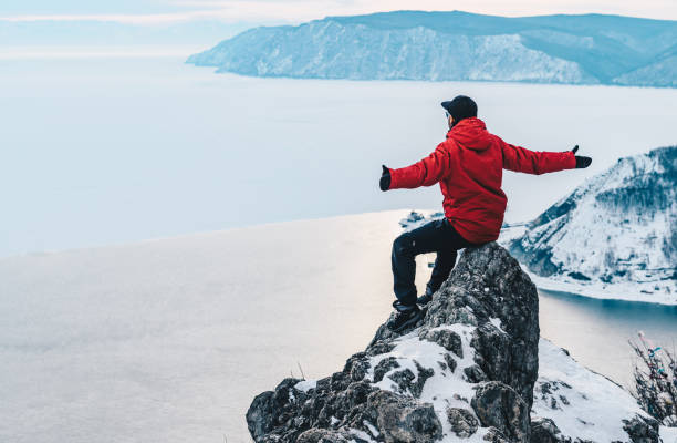 tourist sitzt auf tscherski stein und mit blick auf den baikalsee und angara fluss fließt in listvyanka ein kleines resort township am ufer des baikalsees, russland. - baikalsee stock-fotos und bilder