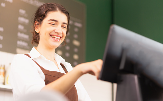 Beautiful caucasian barista woman happy to make coffee order on cashier screen at coffee bar. Barista work at coffee bar and food service business
